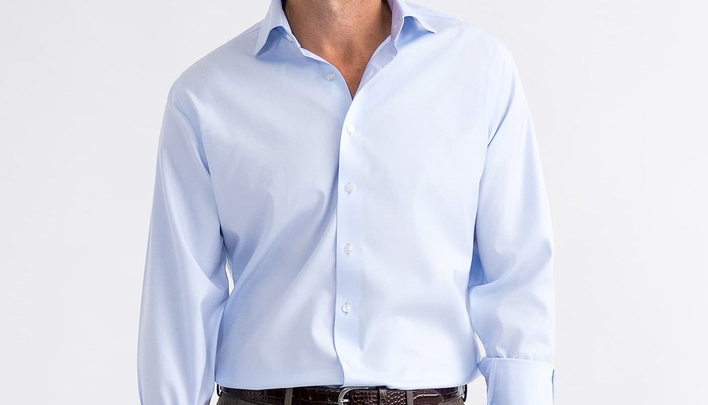 Homem vestindo uma elegante camisa social branca confeccionada sob medida da marca Perffeto Alfaiataria. O homem está vestindo também um grava azul escuro.